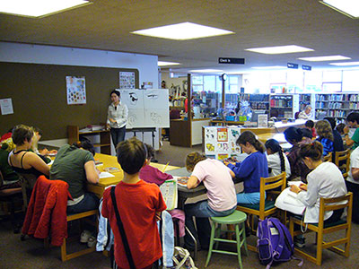 Mei teaching students a how to draw art lesson in a library.